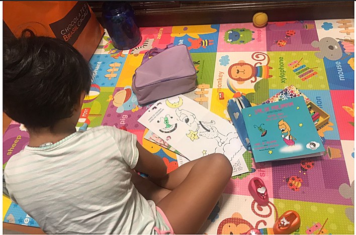 Uma criança sentada num tapete colorido, com o livro O Sol de Pirlimpim e um material de atividades ao lado