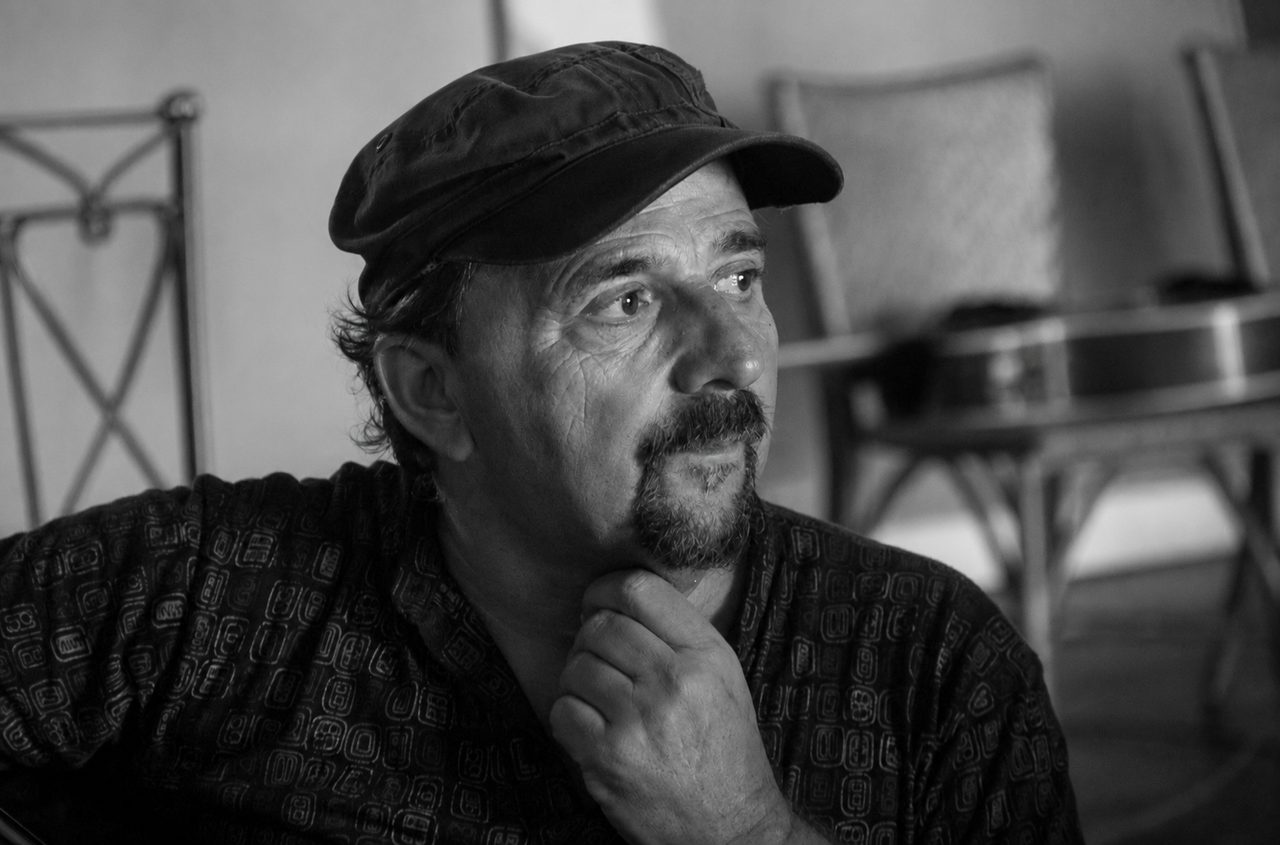 Retrato em preto e branco de Carlinhos Antunes, de boina, mão no queixo, olhando pensativo para o lado