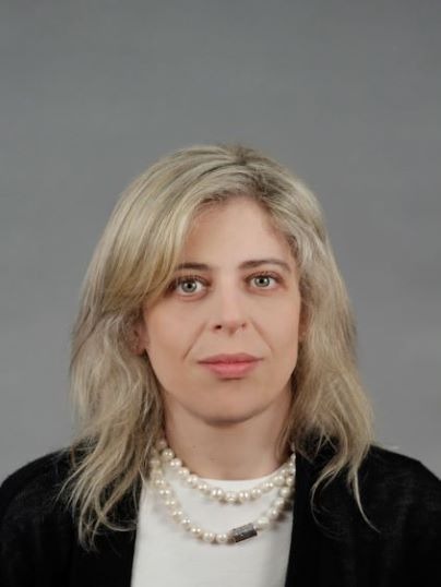 Retrato de Mafalda Miranda Barbosa: cabelos loiros sobre os ombros, casaco escuro sobre blusa branca e colar de pérolas, diante de um fundo cinza